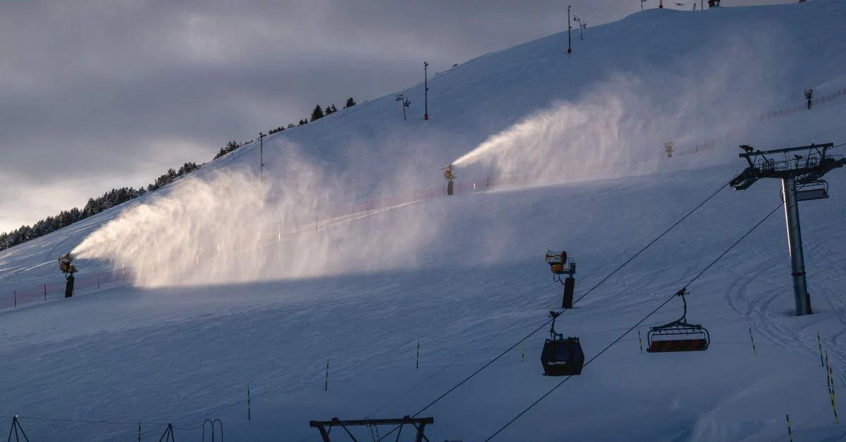 Symbolbild: Mehrere Schneekanonen beschneien einen Skipistenhang; rechts ist ein Skilift zu sehen.