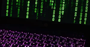 Symbolbild: Ein beleuchtetes Laptop mit Tastatur zeigt grüne Zeichen auf dem Bildschirm.
