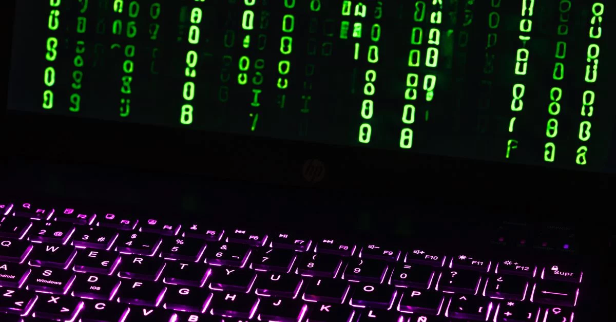 Symbolbild: Ein beleuchtetes Laptop mit Tastatur zeigt grüne Zeichen auf dem Bildschirm.